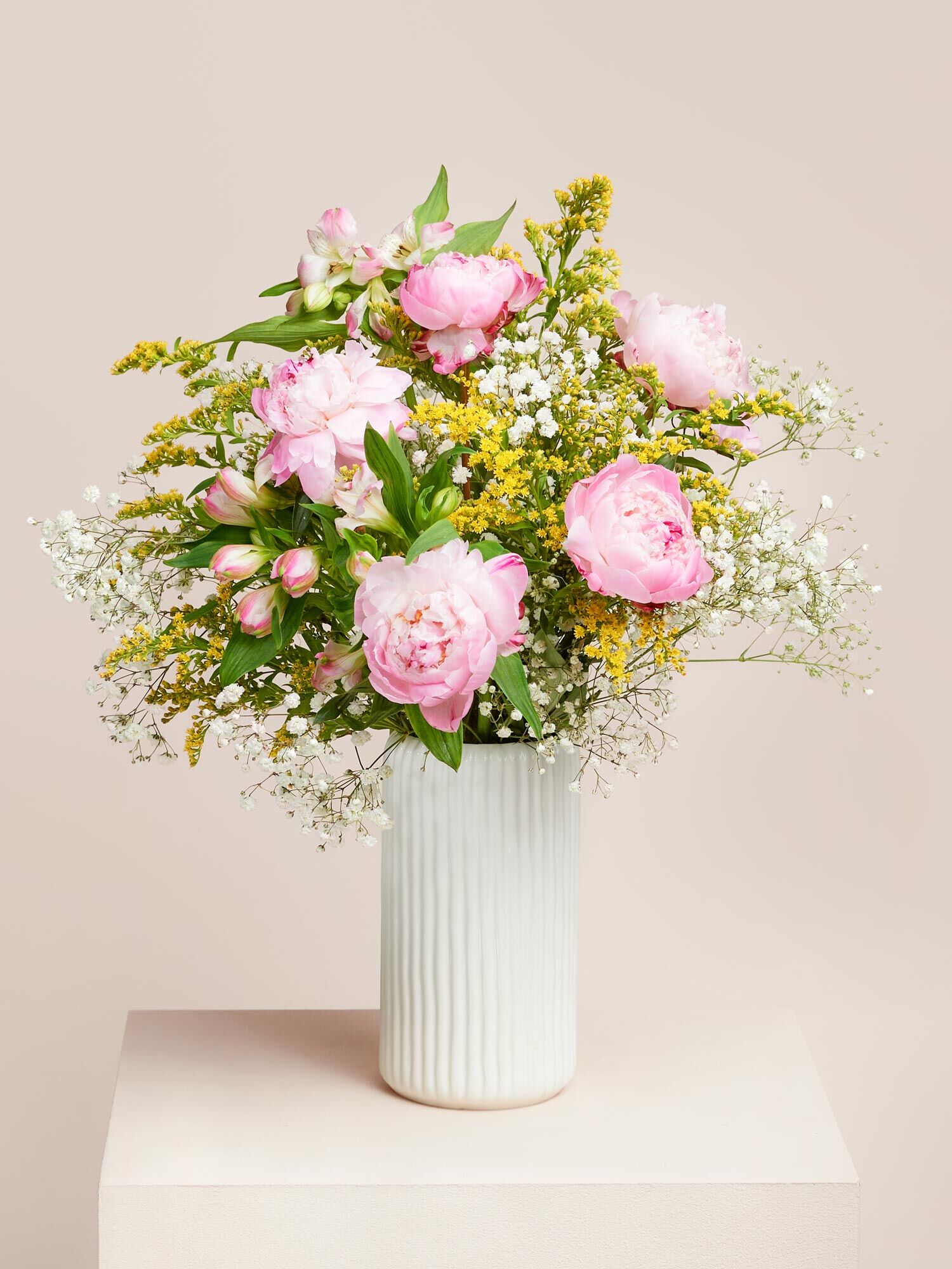 Rosafarbene Pfingstrosen, arrangiert mit Schleierkraut und gelbem Beiwerk in einer hellen, schmalen Keramikvase