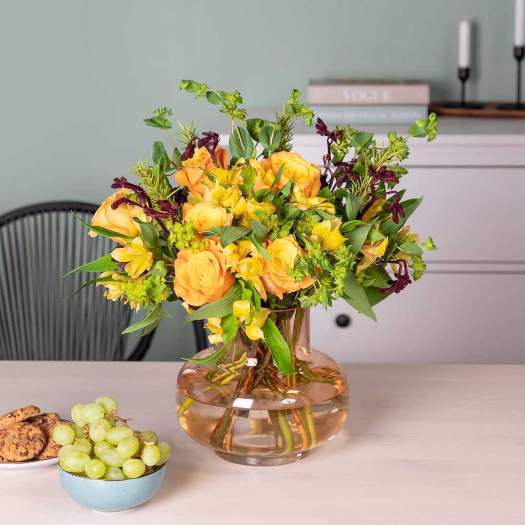 Blumenstrauß mit gelb und grünen Blüten in orangener Glasvase auf dem Tisch im Wohnzimmer