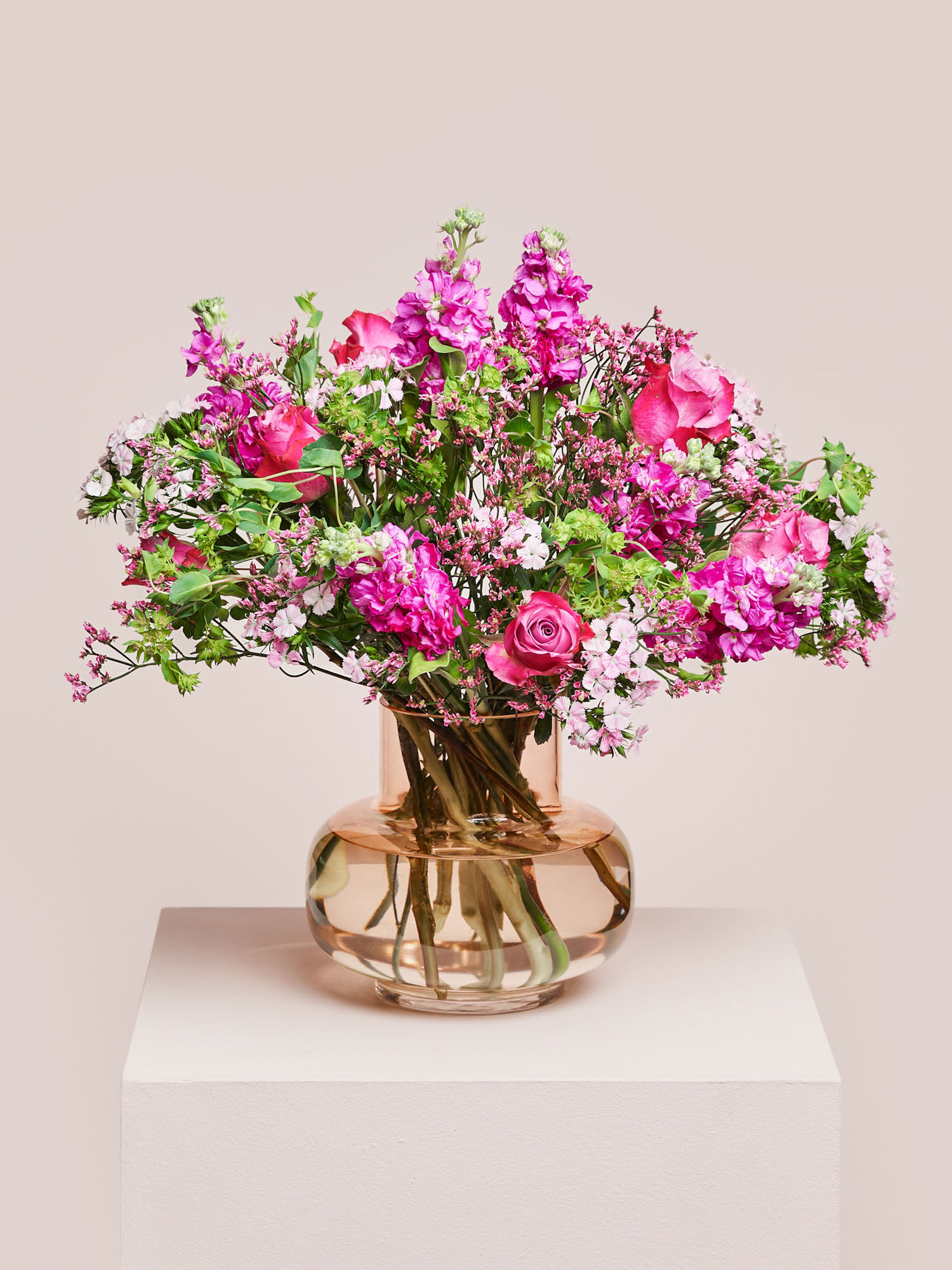 Ein Blumenstrauß mit pinken Rosen, Levkojen, Bupleurum arrangiert in einer Glasvase