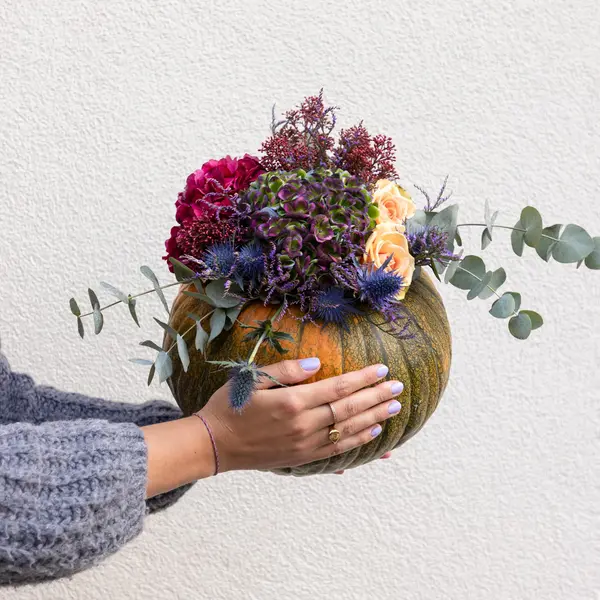 Kürbis der von Händen gehalten wird, der mit Blüten gefüllt ist