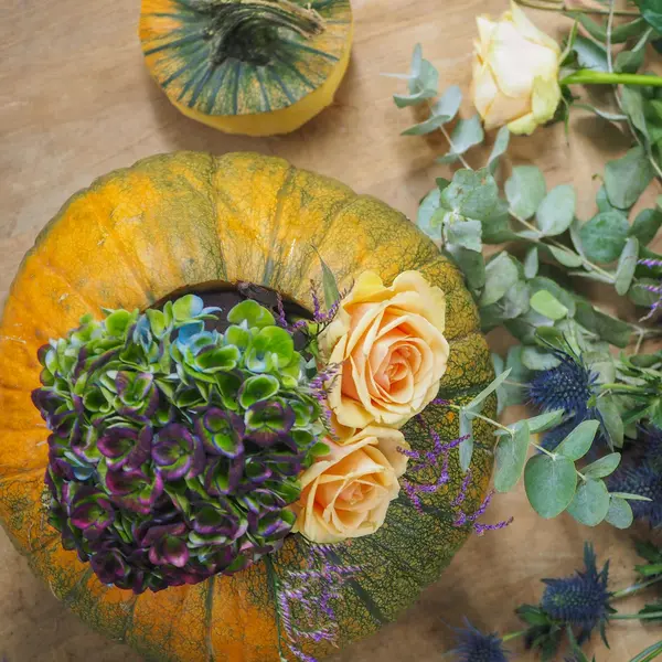 ausgehöhlter Kürbis, der mit Steckschaum gefüllt, in den frische Blüten gesteckt sind, in der Vogelperspektive