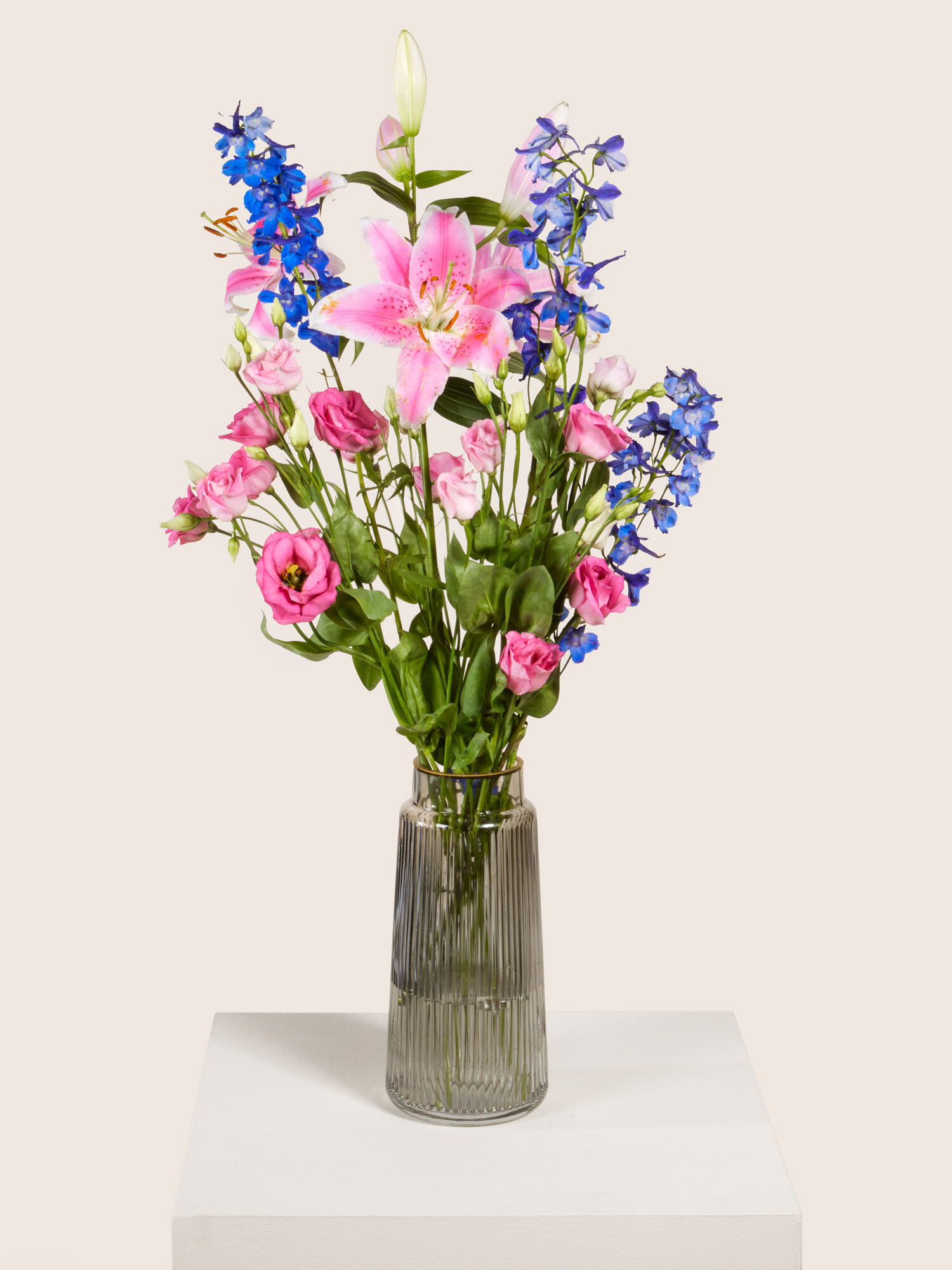 Rosafarbene Lilien, Pinke Eustoma und blauer Rittersporn, arrangiert in eine hohe Glasvase