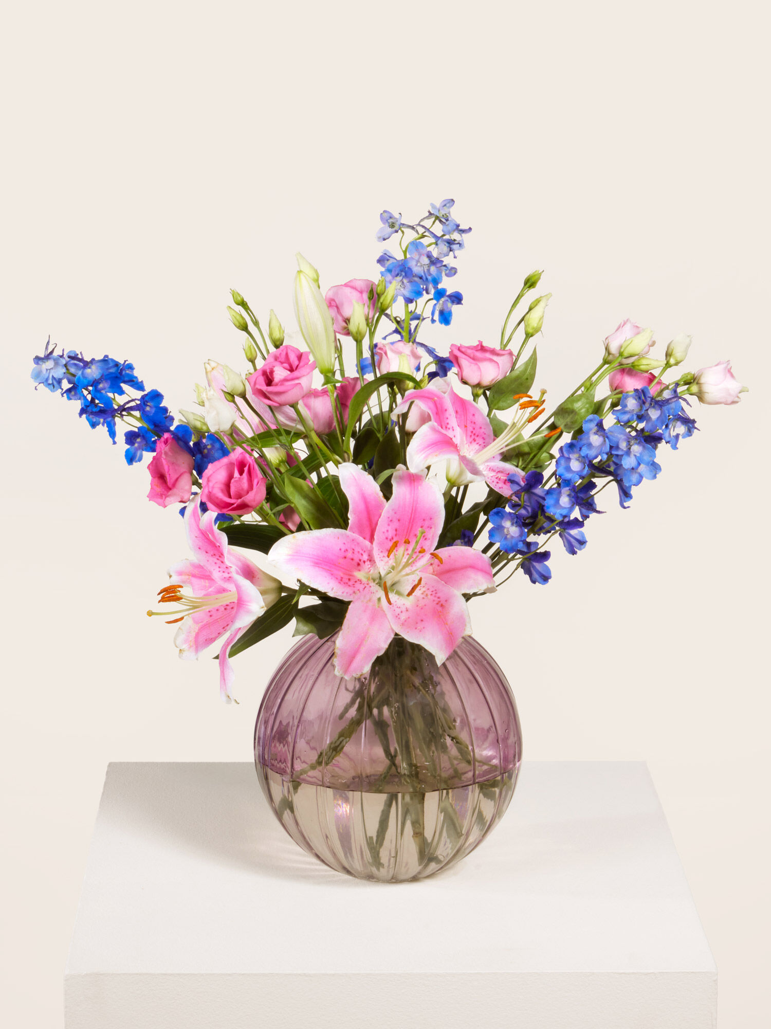 Rosafarbene Lilien, Pinke Eustoma und blauer Rittersporn, arrangiert in eine Kugelglasvase