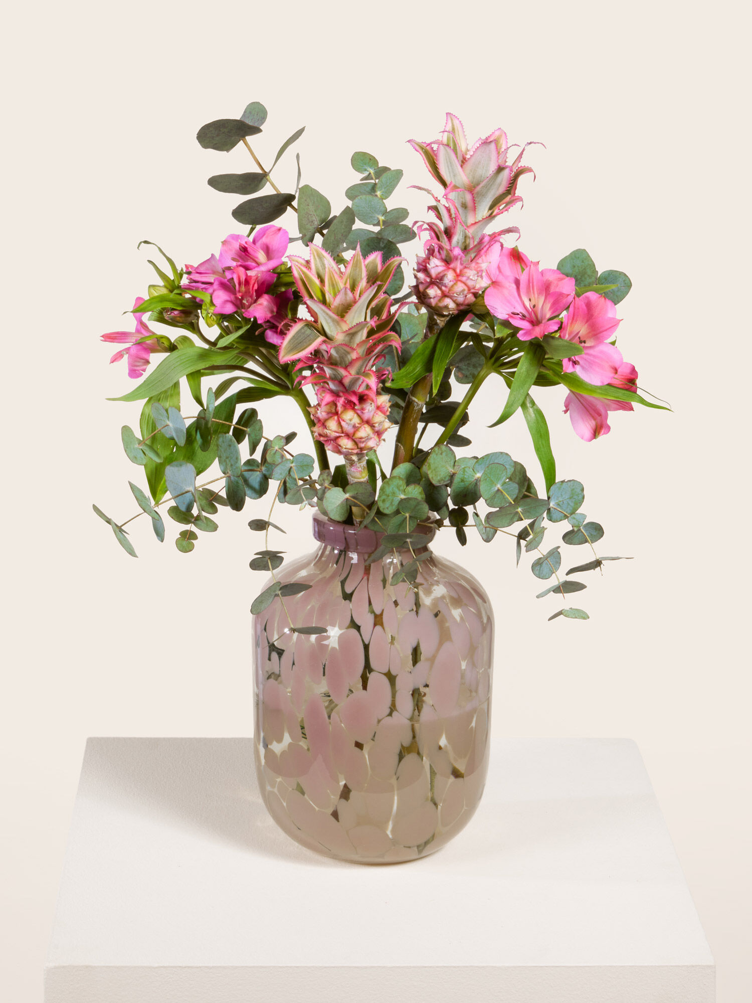 Tropical Crush Baby Ananas, mit pinken Alstromerien und Eukalyptus, arrangiert in eine Glasvase mit rosafarbenen Flecken