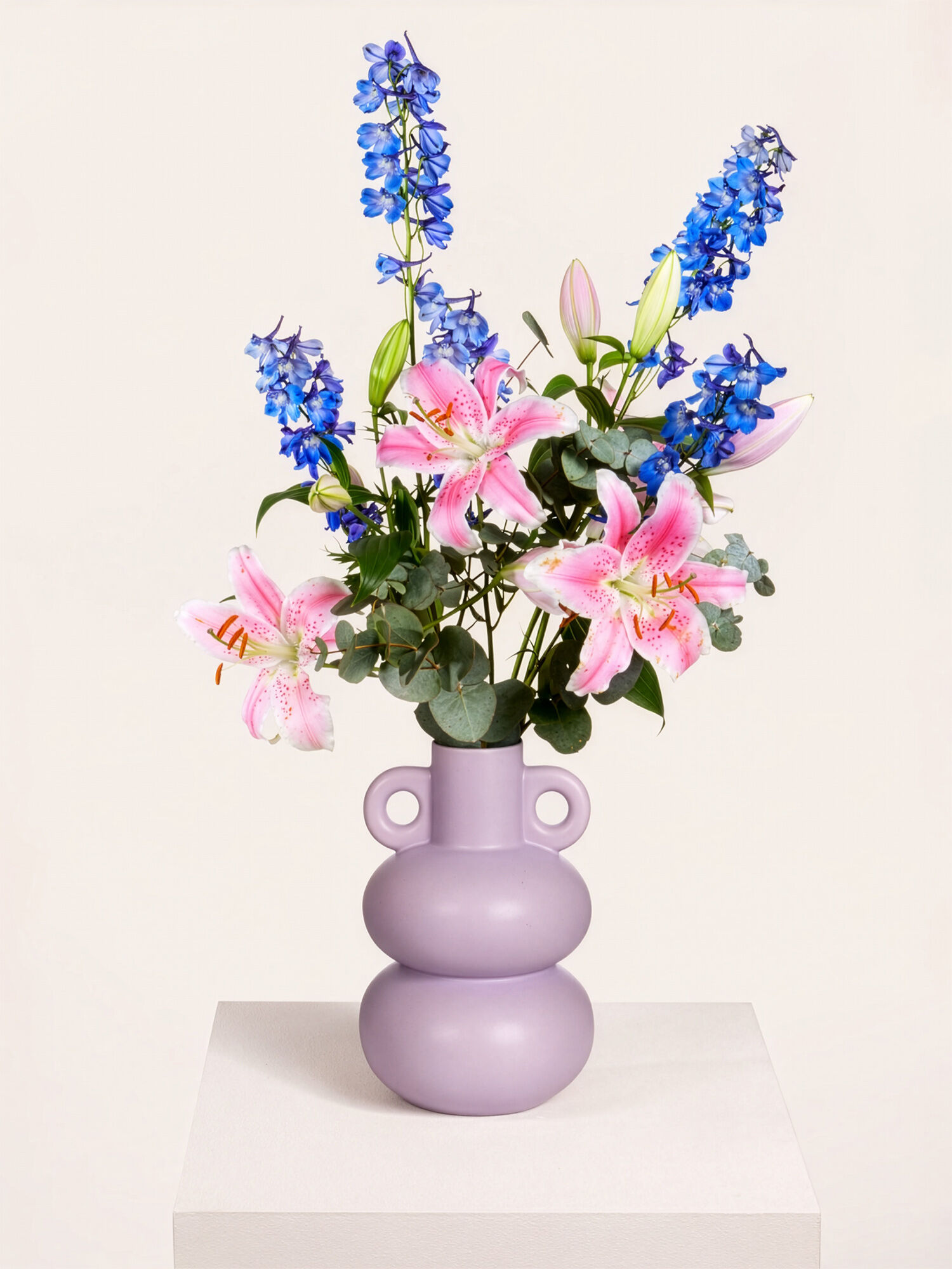 Blumenarrangement, rosa Lilien, blaue Delphinium, Lavendelfarbene Vase, glänzende Vase