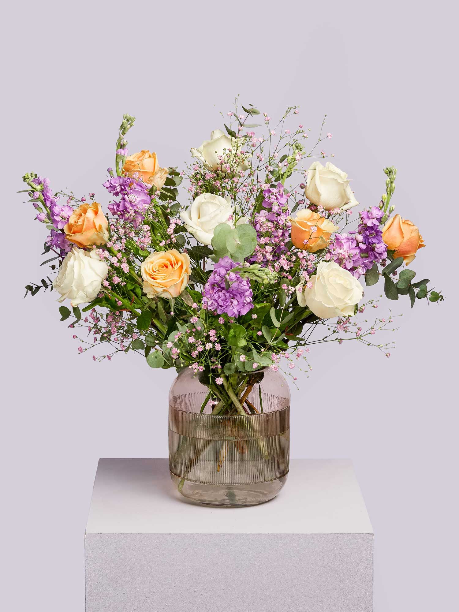 Ein lieblicher Blumenstrauß, bestehend aus Rosen, lilafarbenen Levkojen, Eukalyptus und Beiwerk, arrangiert in eine Glasvase